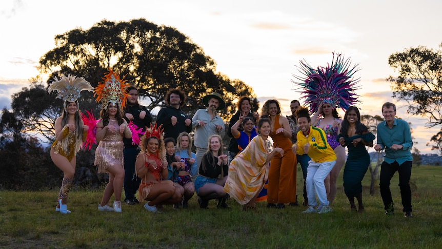 A group of performers in different elaborate costumes stand in the bush.