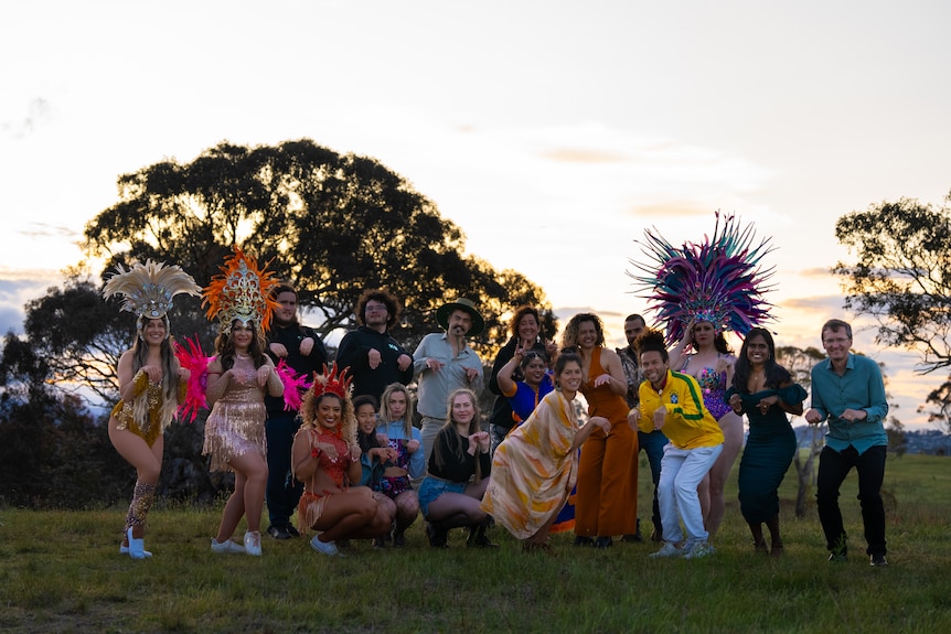 A group of performers in different elaborate costumes stand in the bush.