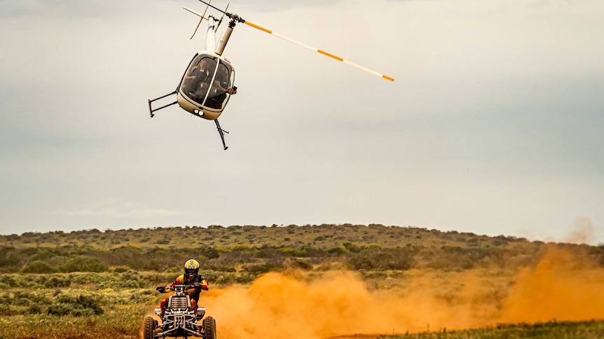 A helicopter flies above an ATV racing through the desert.