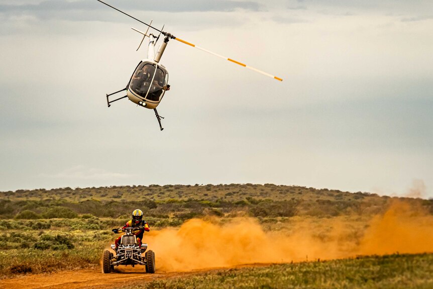 An ATV bike races through the Gascoyne whilst a helicopter fly's overhead.