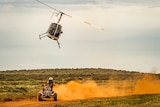 A helicopter flies above an ATV racing through the desert.