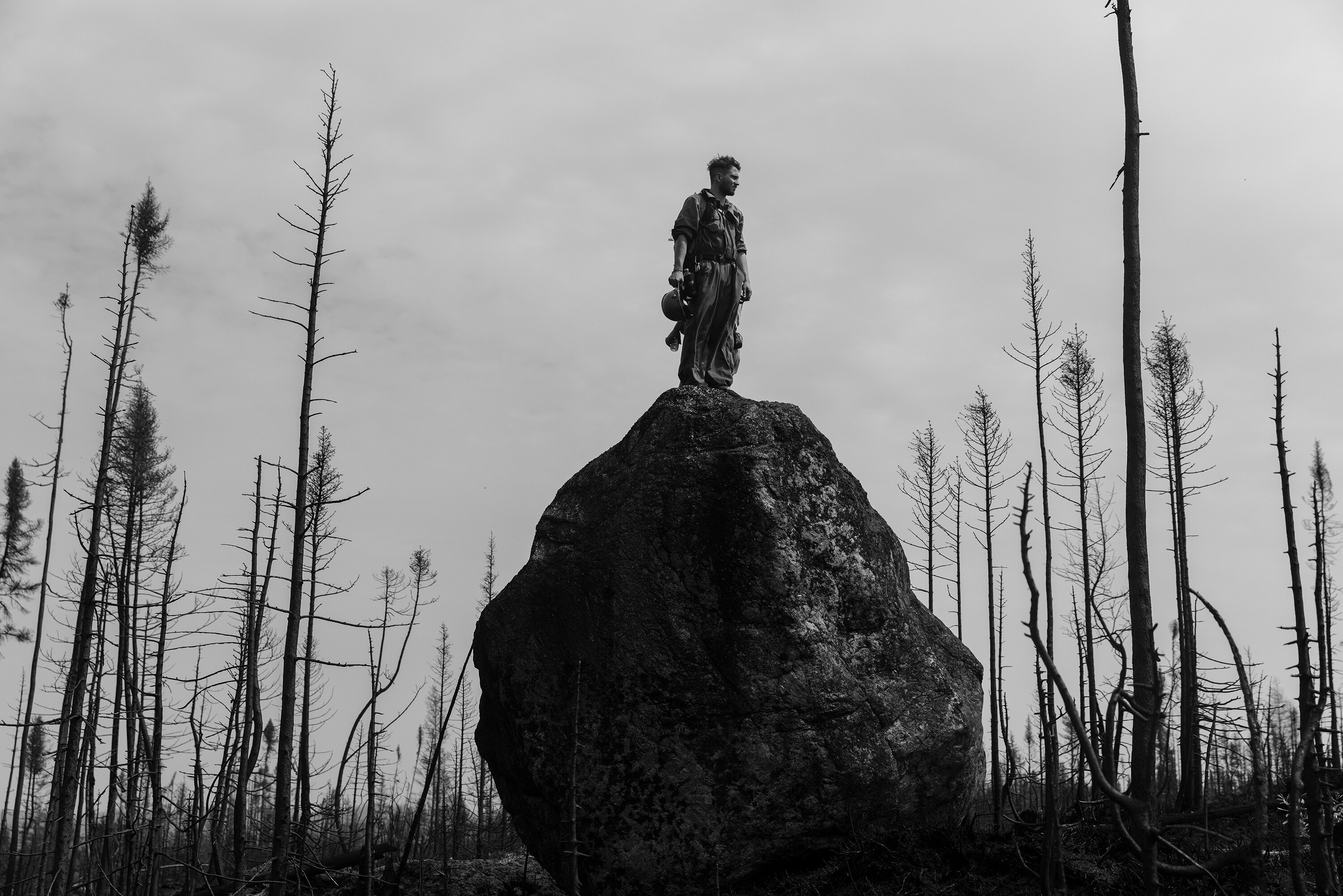 A black and white image of a man standing on a rock in a burnt landscape