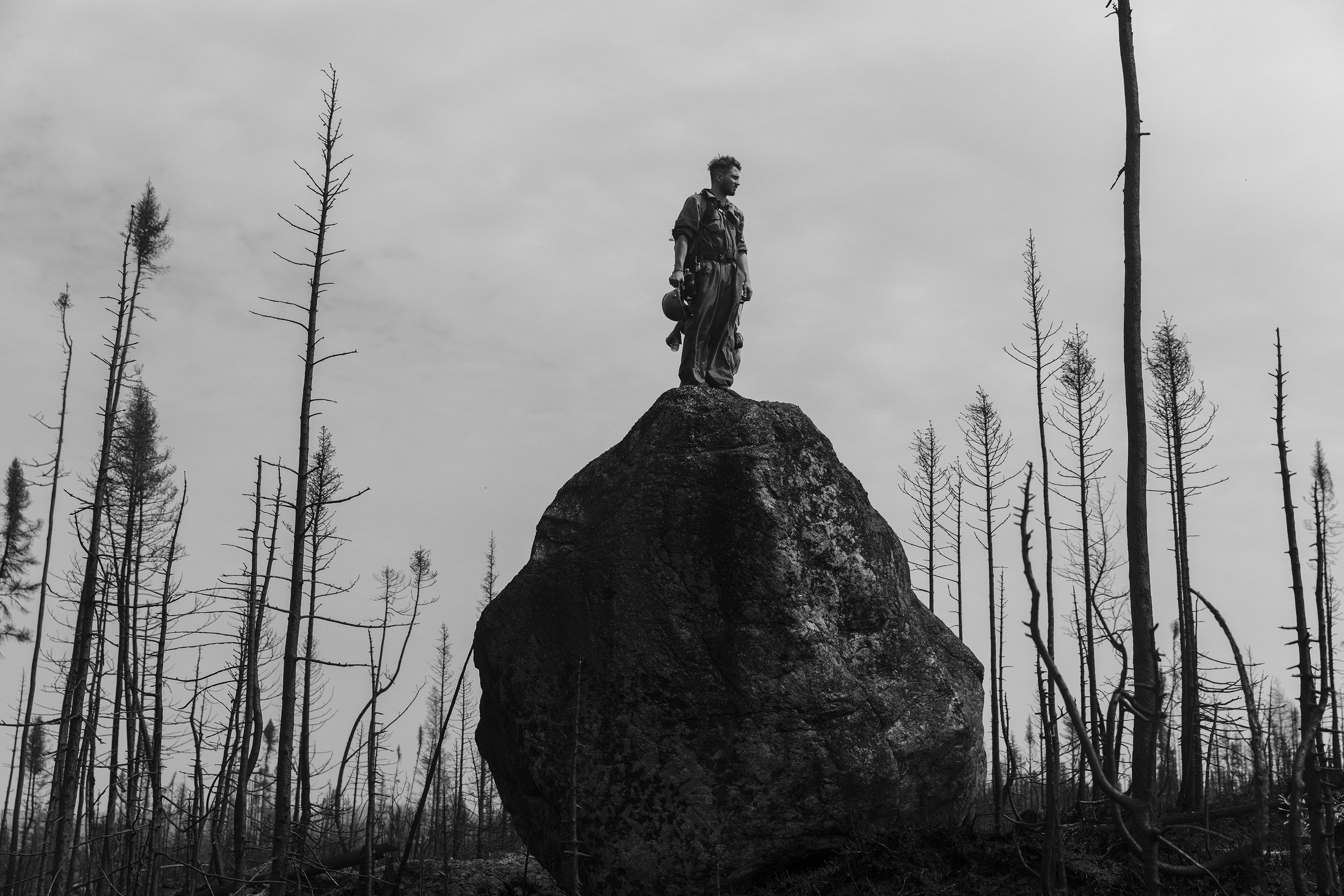 A black and white image of a man standing on a rock in a burnt landscape
