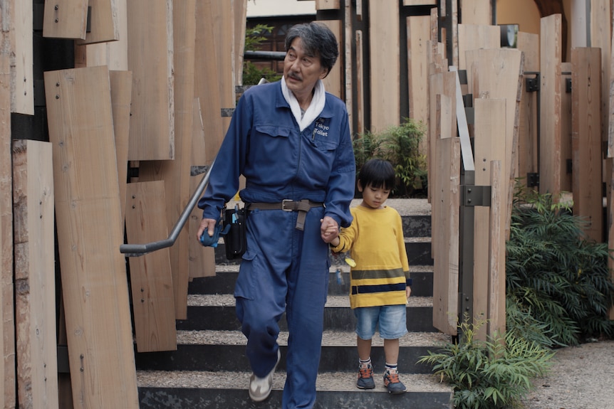 A film still of Kōji Yakusho holding the hand of a boy Kisuke Shimazaki, dressed in yellow.