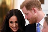 Prince Harry turns to Meghan Markle, speaking in her ear, as she smiles.