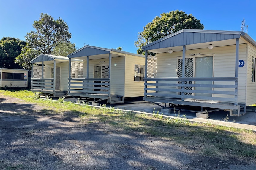 Three cabins in a row, in an old caravan park, on a sunny day.