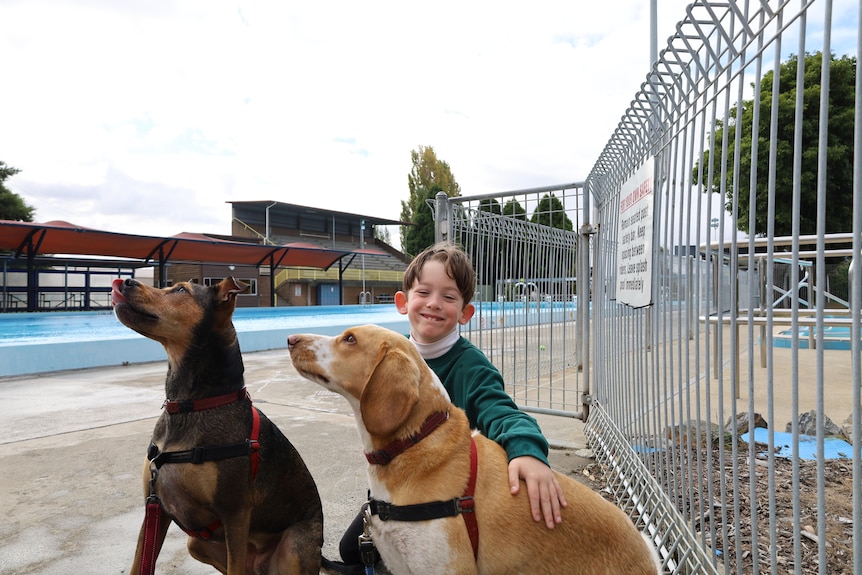 Riley Tybell smiles as he pats two dogs next to the Glenorchy pool.