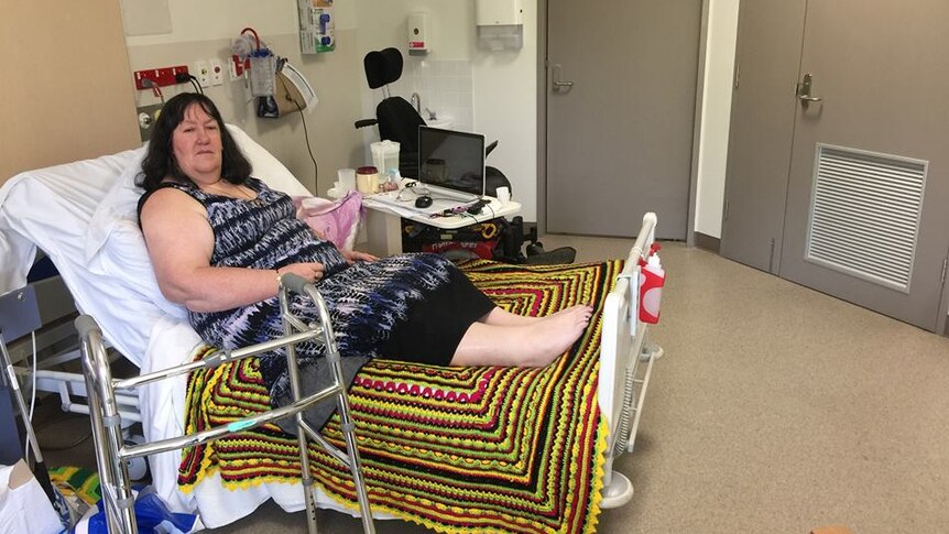 A woman on a bed in a hospital room with a walker next to her.