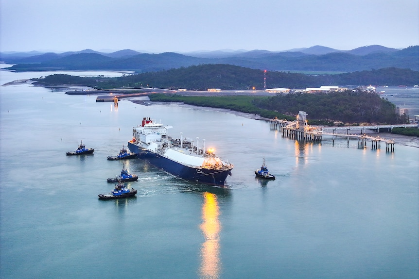 Vista aérea de un gran petrolero remolcado por varios remolcadores en un puerto 