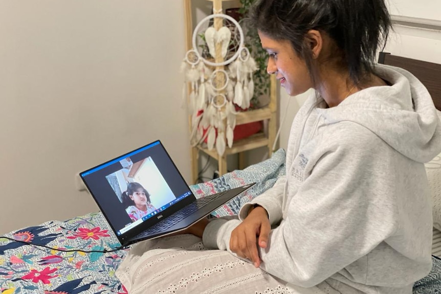 Divya sitting on a bed and videochatting with her daughter in India