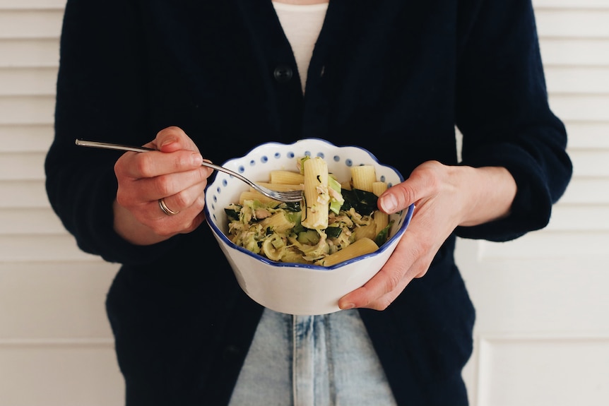 Hands holding a bowl of tuna rigatoni pasta with zucchini, basil and lemon juice, a quick and easy recipe.
