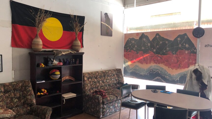 A room with an Aboriginal Flag on left-hand wall, Indigenous art on right-hand wall, shelves, armchairs and a table