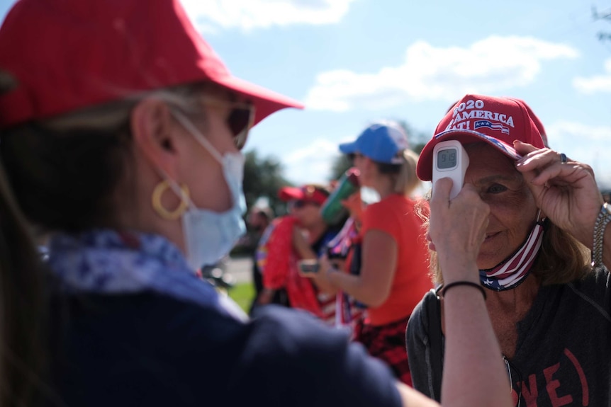 A woman in a MAGA hat getting a temperature check