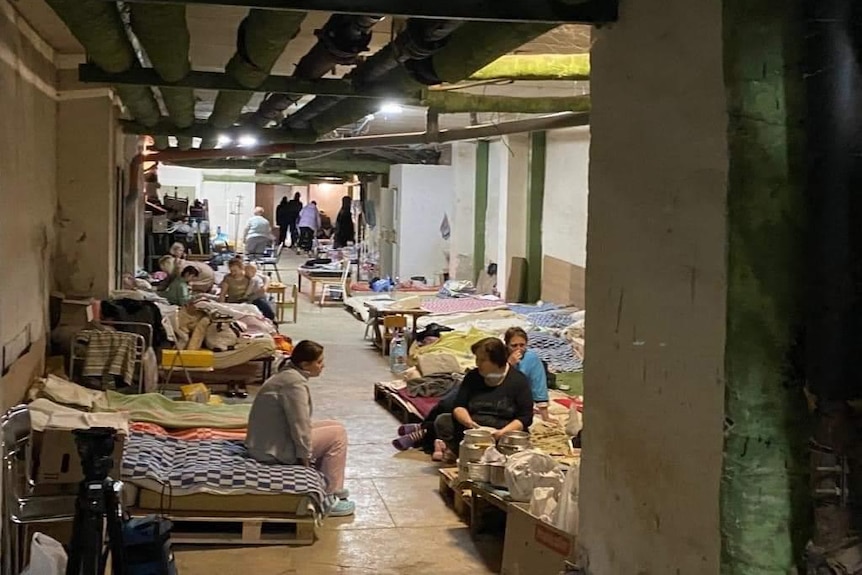 People sit in a bunker in Ukraine in a sparse covered room with stretches and a few items around