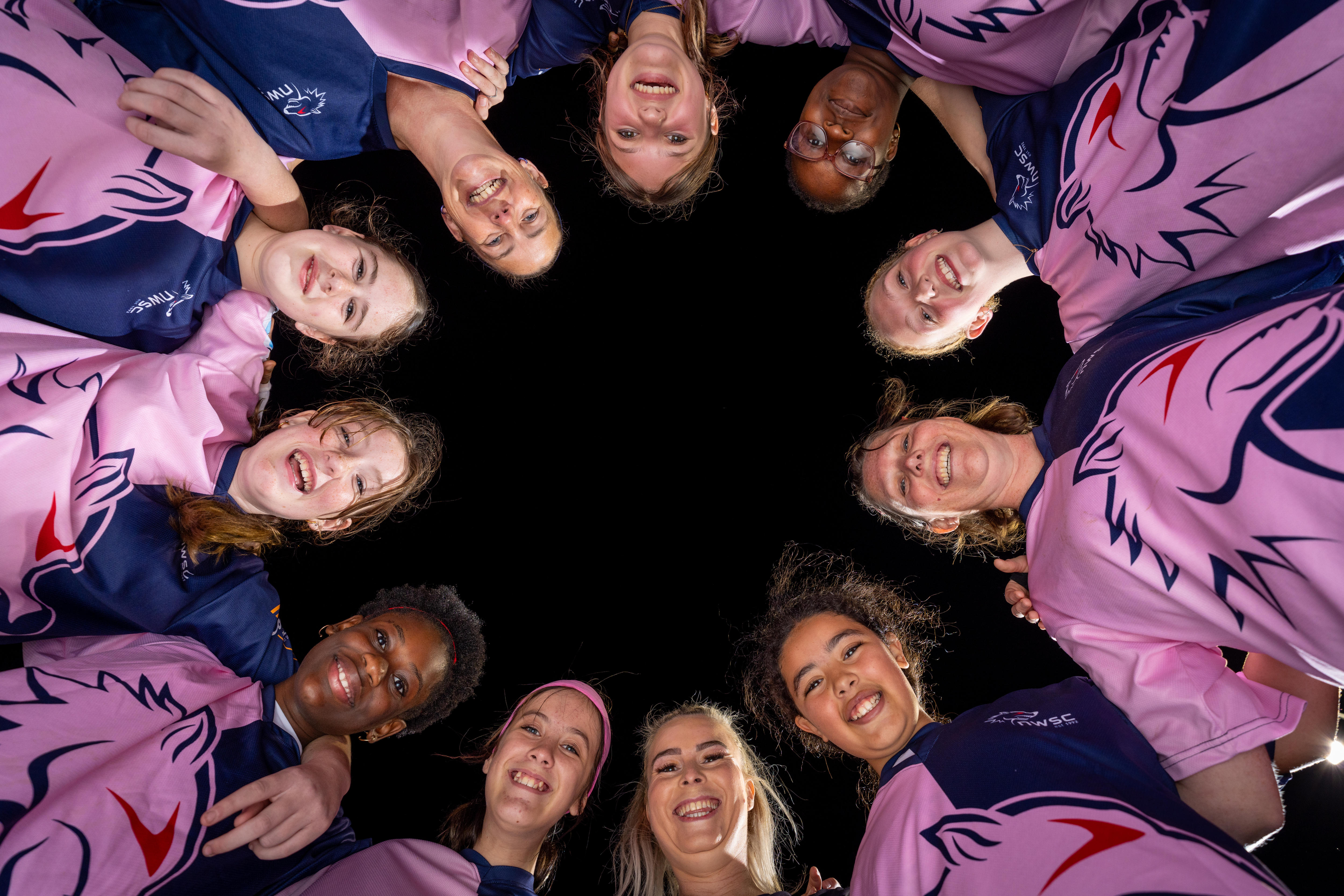 A ring of girls stand in a circle and look down.
