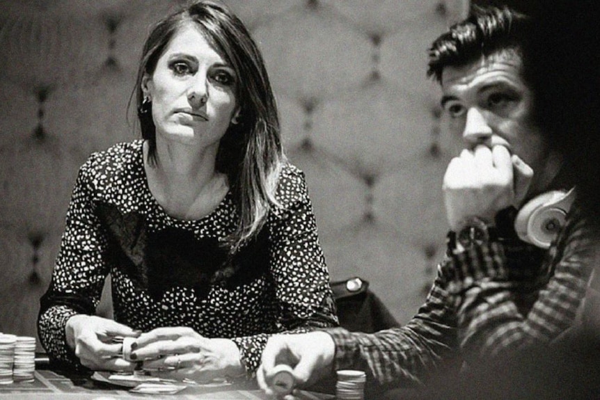 Black and white image of Alex O'Brien sitting at table holding poker chips, with man seated to her right holding.