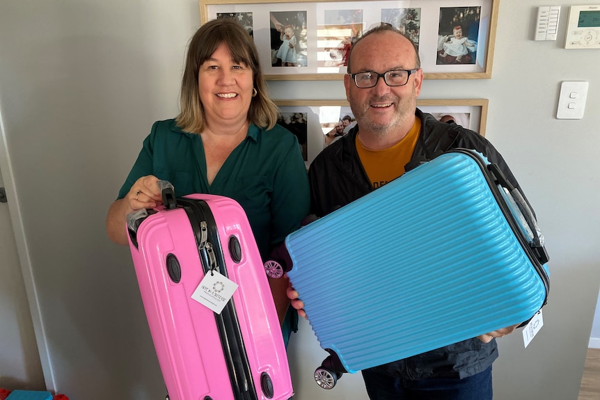 Man and woman holding up a blue and pink suitcase.