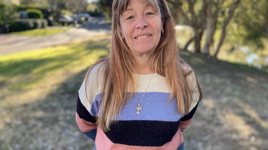 A woman smiles while holding her hands behind her back.