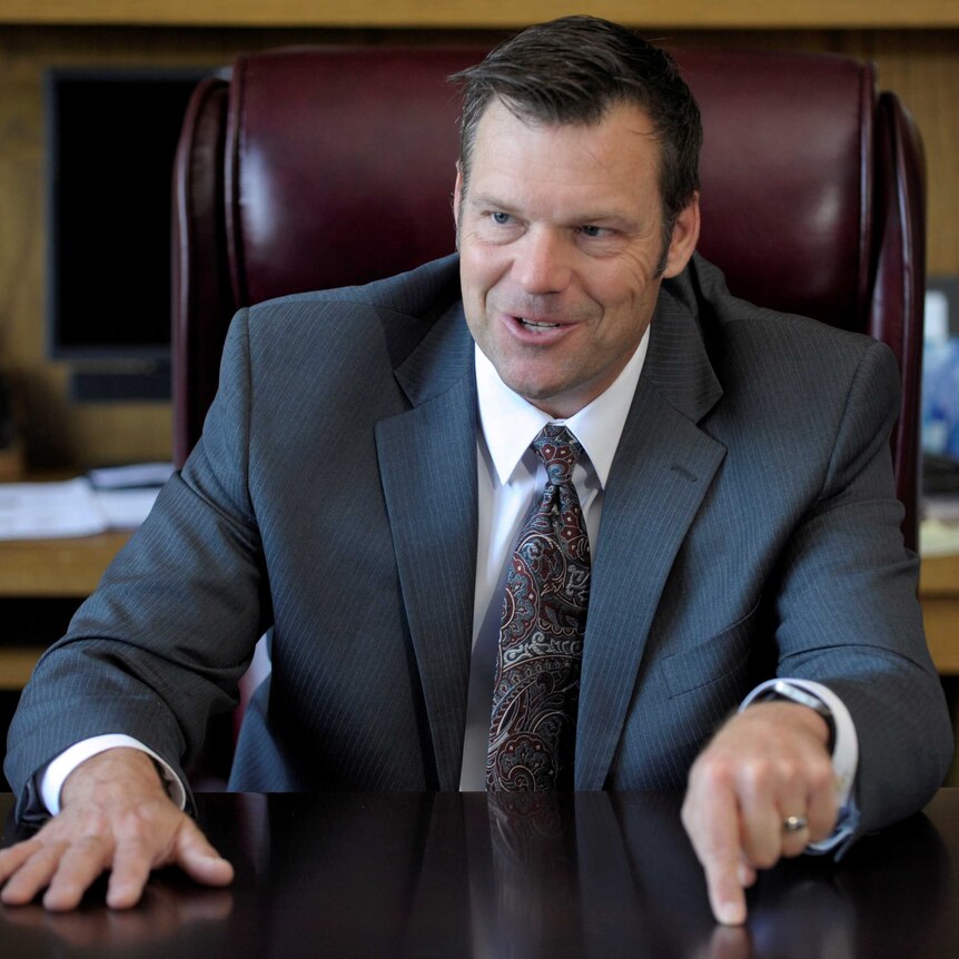 Kris Kobach stabs his finger into his desk to makes a point