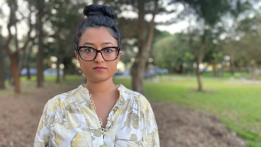 a woman wearing glasses standing outdoors in a park