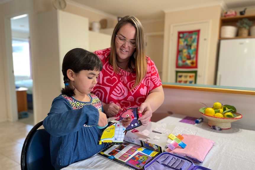 A mother doing a puzzle with her young daughter over the kitchen table. 