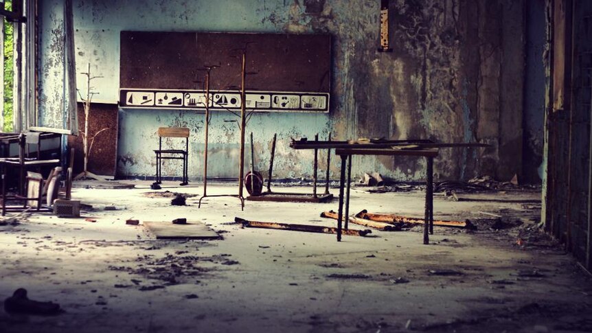 A destroyed class room with a blackboard at the back of the room and pieces of metal littered on the floor.