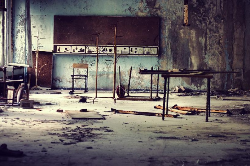 A destroyed class room with a blackboard at the back of the room and pieces of metal littered on the floor.