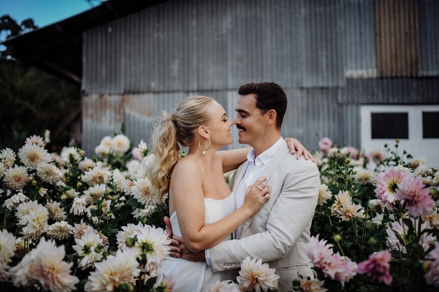a bride and groom stand in a garden bed surrounded by flowers