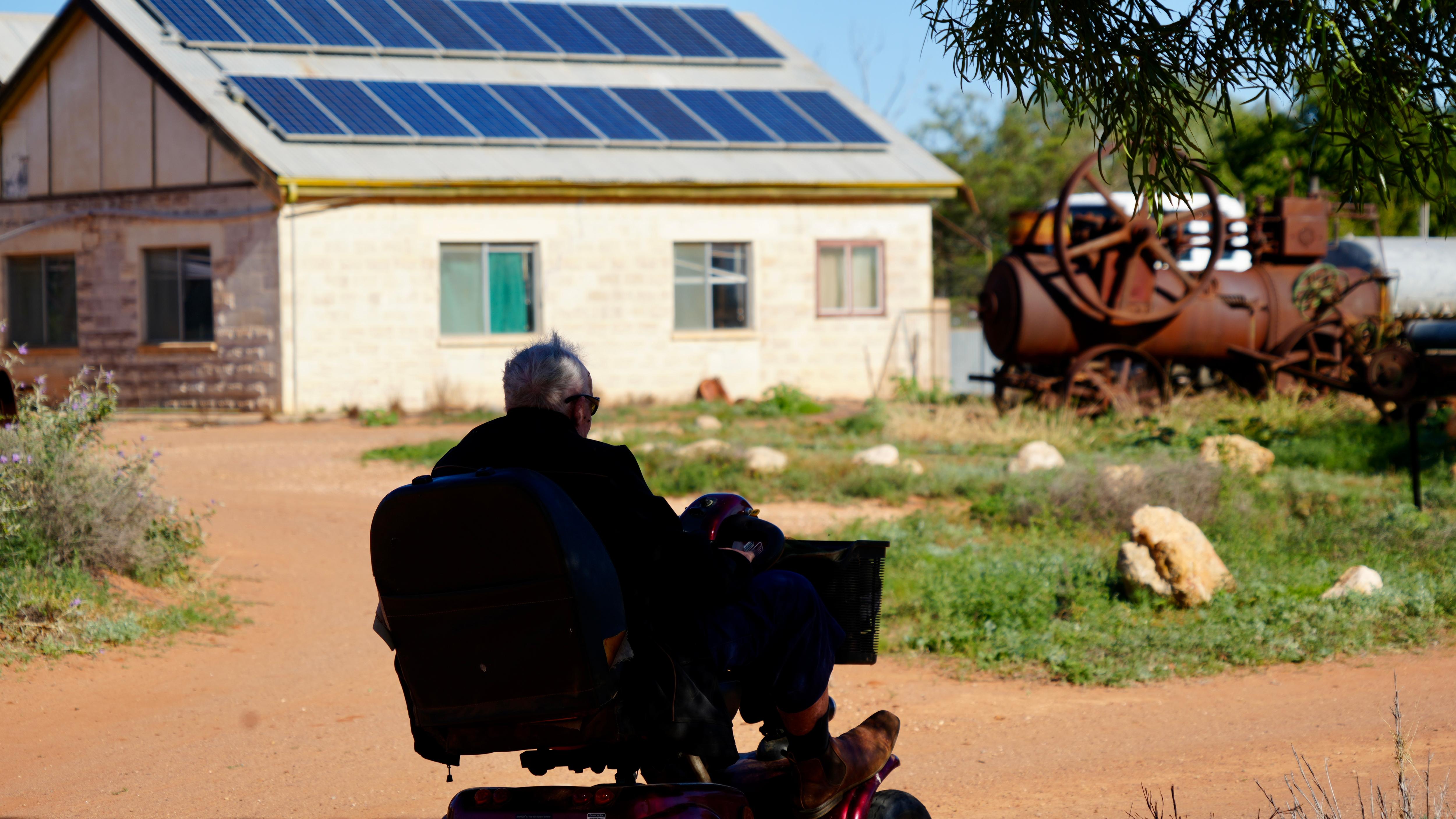 a shadow of a man driving a red gopher with a large brick shed in the background 