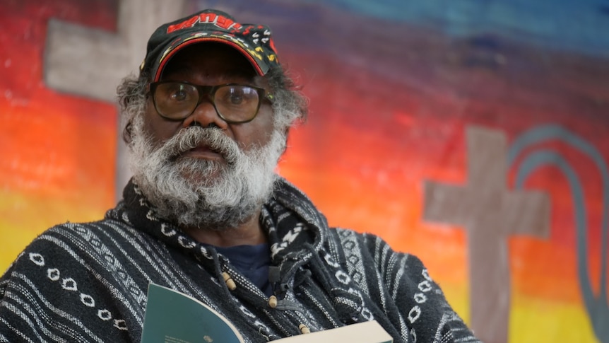 Indigenous pastor Geoffrey Stokes sitting with a bible in his hands, in front of a bright background