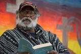 Indigenous pastor Geoffrey Stokes sitting with a bible in his hands, in front of a bright background