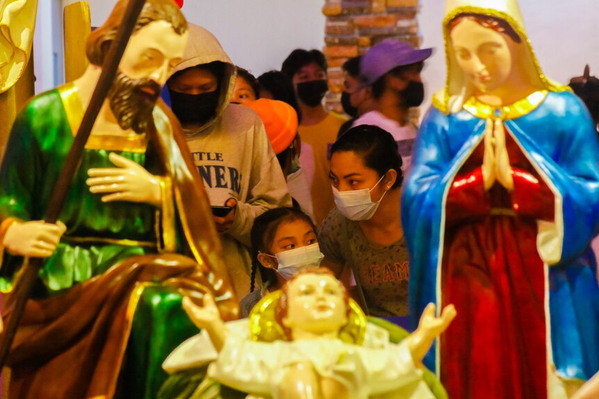 People wearing face masks stand with statues at a church in the Philippines