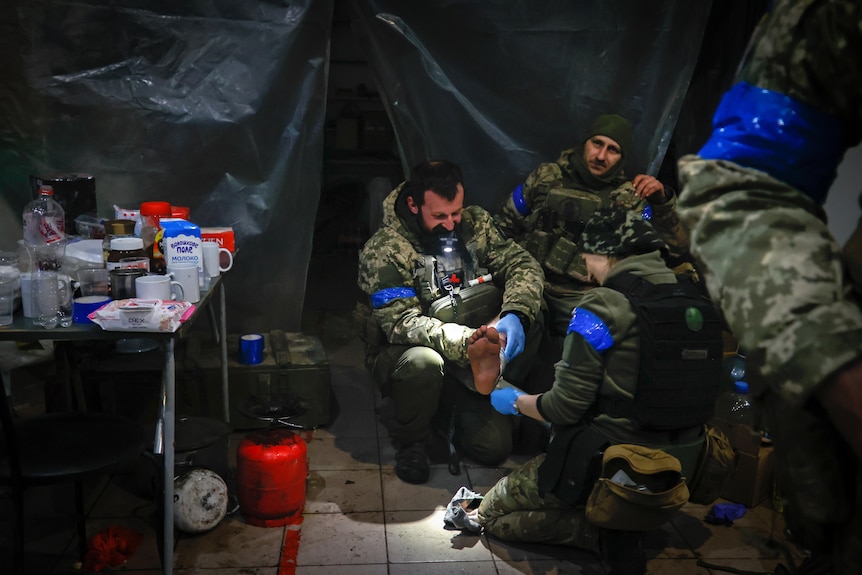 A group of soldiers in a tent wearing bright blue tape around their arms over heavy camo gear.