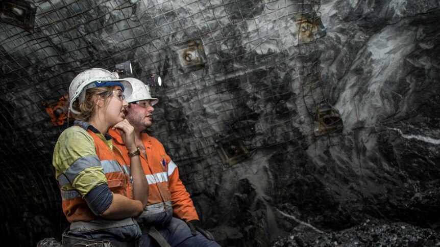 Two geologists standing next to each other having a discussion in an underground gold mine.