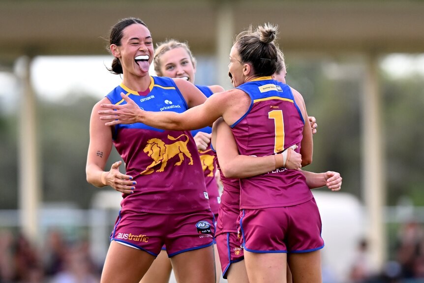 A Brisbane AFLW player sticks her tongue out at her teammates as she celebrates a goal against Collingwood.