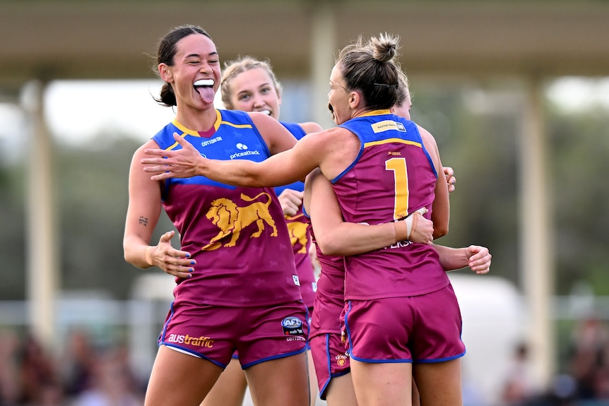 A Brisbane AFLW player sticks her tongue out at her teammates as she celebrates a goal against Collingwood.