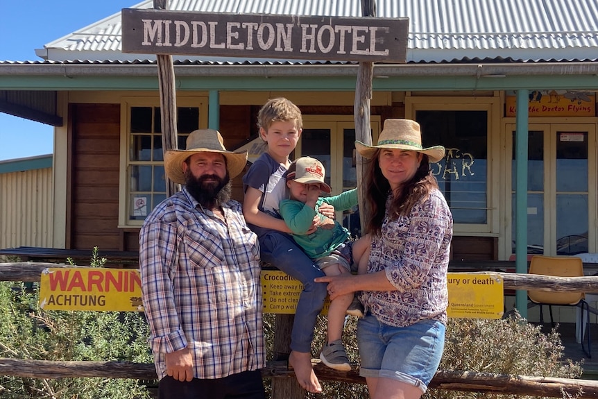 A family of four pose for a family picture in front of an old outback pub, under a sign that says Middleton Hotel.