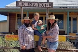 A family of four pose for a family picture in front of an old outback pub, under a sign that says Middleton Hotel.