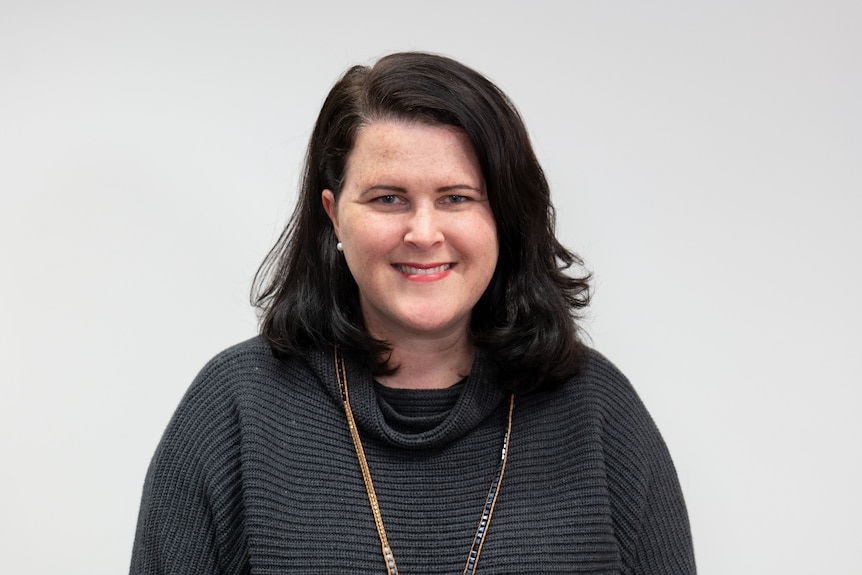 A woman in a black jumper smiling at the camera with a white background