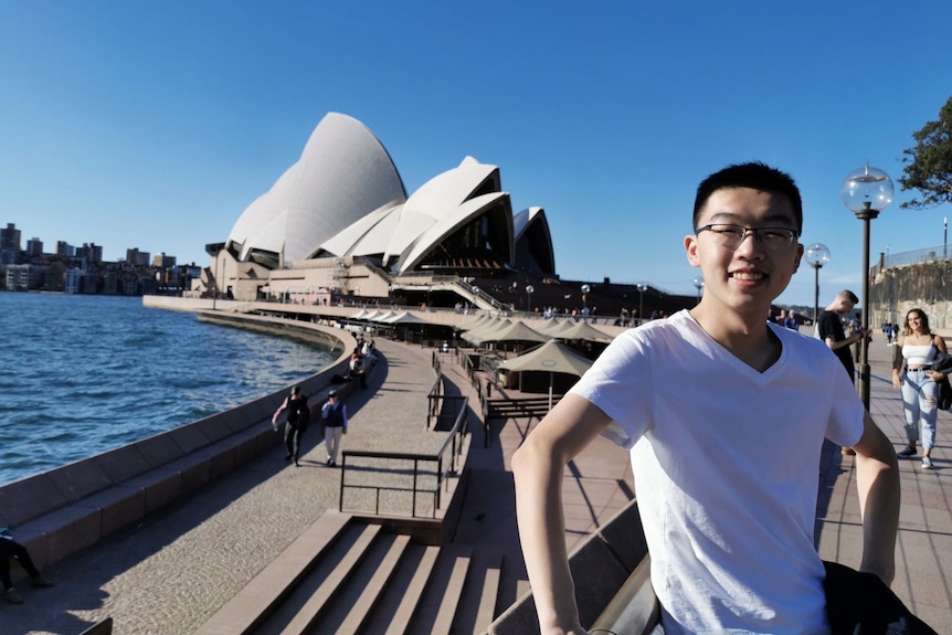 A young Chinese man standing in front of Sydney Opera House. 
