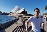 A young Chinese man standing in front of Sydney Opera House. 