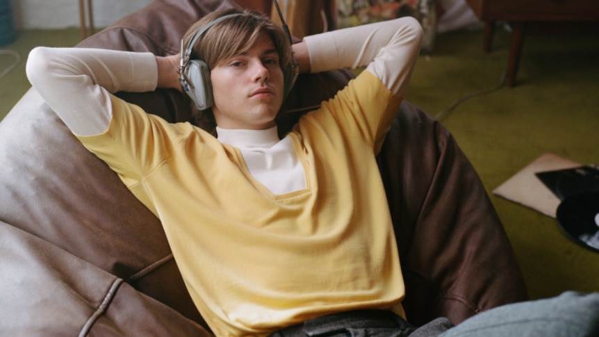 Press image of Ruel; wearing headphones, yellow sweater, seated in a beanbag