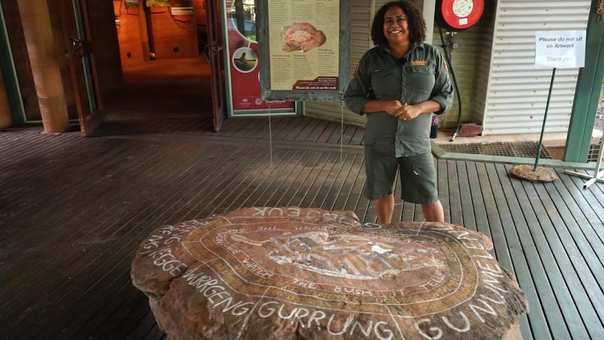 Kakadu Ranger Savana Eccles stands in front of a large rock showing Kakadu Seasons