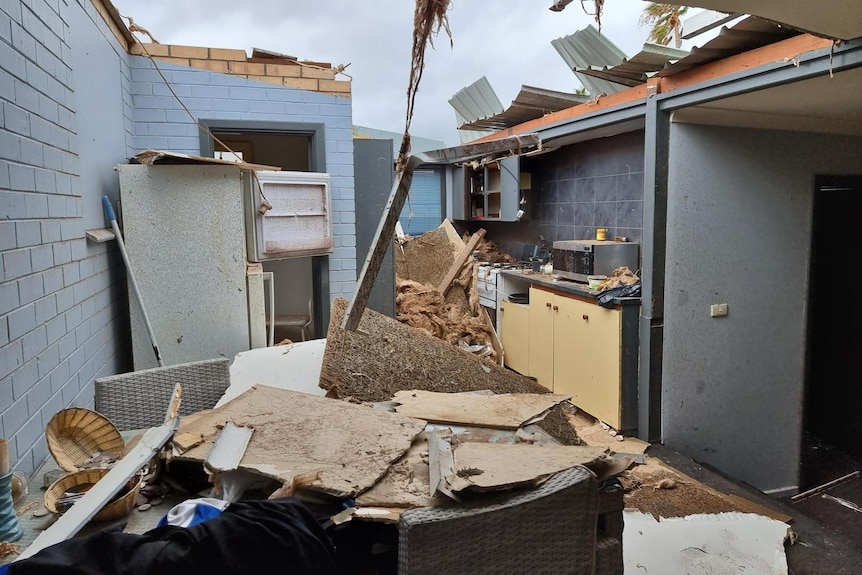 Badly damaged interior of a home with no roof and debris spread throughout the room