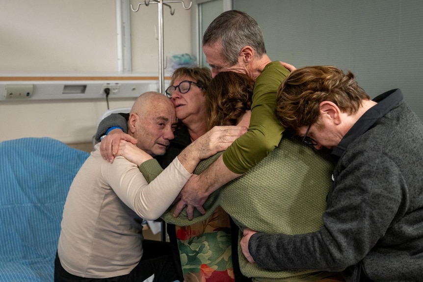 a group hug of the two hostages with three women in a hospital bed