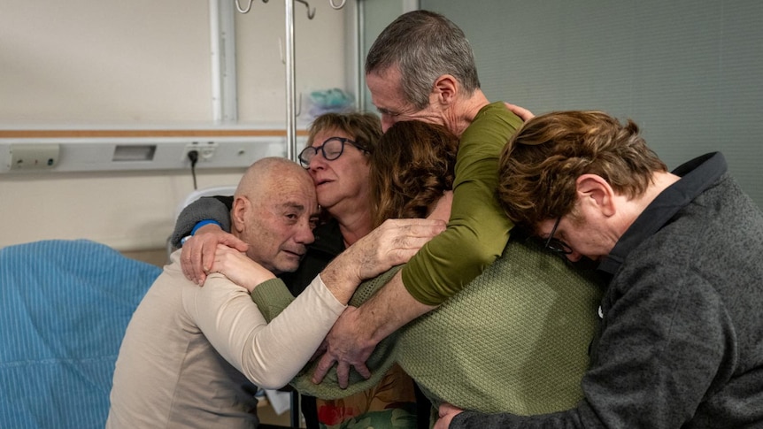 a group hug of the two hostages with three women in a hospital bed