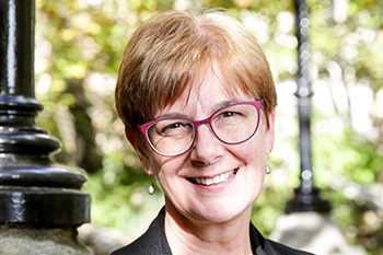 A smiling, bespectacled middle-aged woman with short, auburn hair.