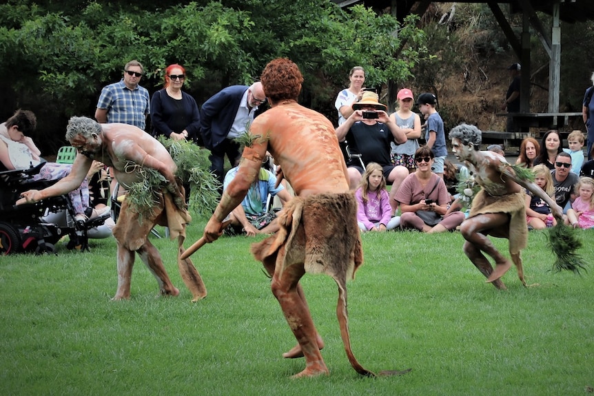 Aboriginal dancers perform, watched by a crowd.