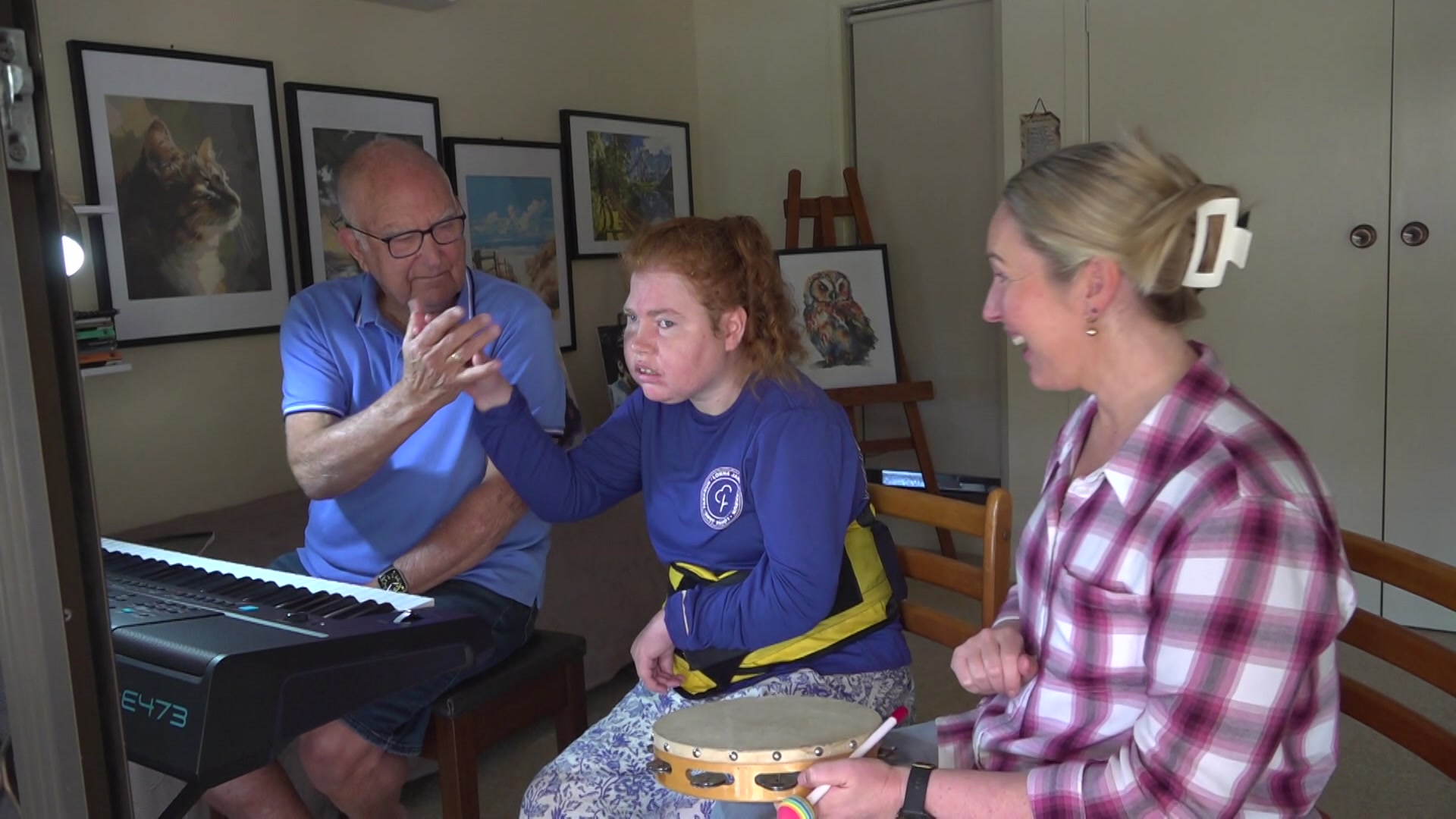 A young woman with a disability high fiving her pop at the piano keyboard with her support worker holding a tambourine 