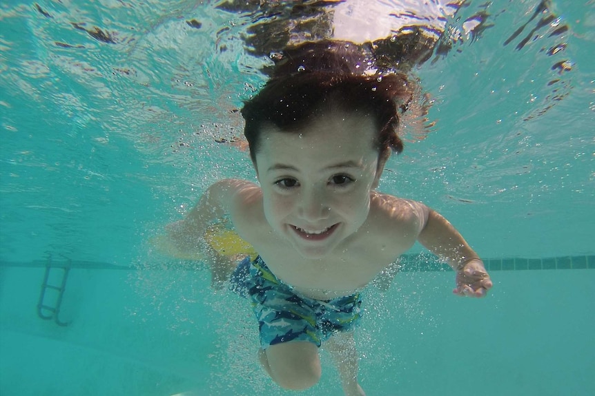 A boy in a swimming pool, viewed from under water.